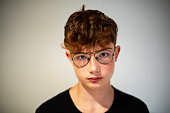 portrait of red-haired teen boy with freckles and eyeglasses on white background