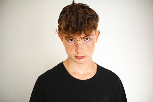 portrait of red-haired teen boy with freckles on white background, medium shot