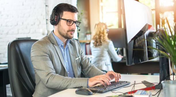 istock Male call centre agent with headset working on computer in office. 1446075702