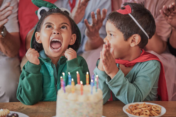 buon compleanno, festa e bimbi in costume di halloween per festeggiare insieme il giorno speciale delle ragazze giovani e divertenti. torta, fantasia e bambino eccitato in un vestito di mostro dinosauro e ragazzo in un mantello da supereroi - birthday family party cake foto e immagini stock