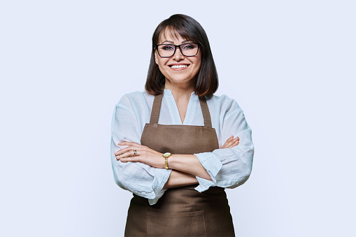 Confident successful middle aged woman in apron looking at camera on white studio background. Smiling 40s female worker entrepreneur, small business owner, service shop occupation management staff