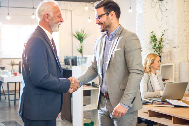 istock Senior executive shaking hands with young employee at office. 1446076219