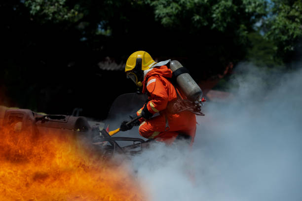 istock Firefighter Rescue training to stop burning flame, Fireman wear hard hat and safety uniform suit for protection burn using axe to break in a car to rescue the trapped driver and passengers. 1446077308