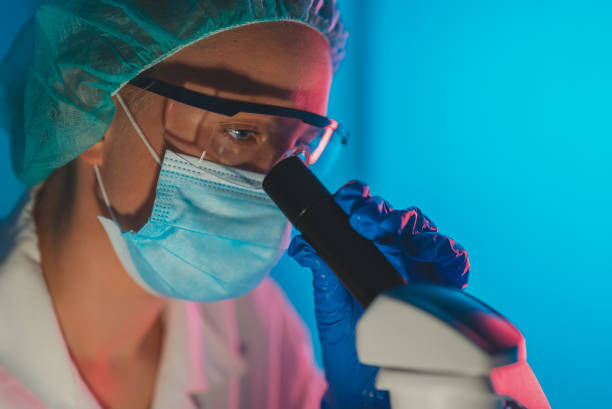 istock Scientist in medical mask working with microscope in lab. 1446079493