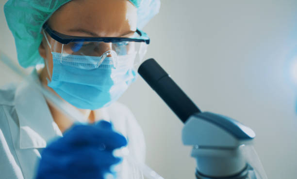 istock Scientist in medical mask working with microscope in lab. 1446079500