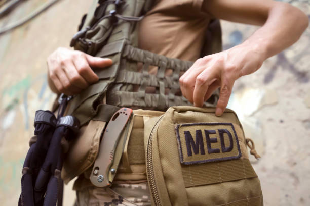 A soldier, a tactical medic opens a first aid kit, close-up view. A doctor in a bulletproof vest, in camouflage, opens a first aid kit, a woman is engaged in tactical medicine and saves lives on the front line, a close-up hand. body armor stock pictures, royalty-free photos & images