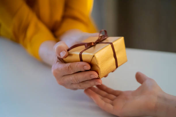 Female hands hold and give a nice packed gift. Female hands hold a gift closeup, top view. A young girl gives a nice packed surprise to her mother, grandmother with love, remembers elderly relatives, visits during holidays, takes care of them. handing out stock pictures, royalty-free photos & images