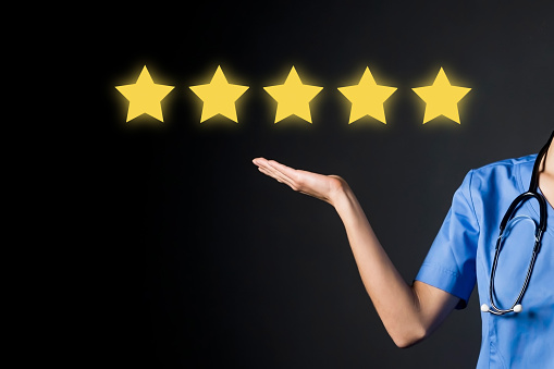 A doctor in a medical suit shows with her hand five stars, the service rating in the clinic, the trust of patients and the competence. A woman medic with a rate of the quality of treatment.