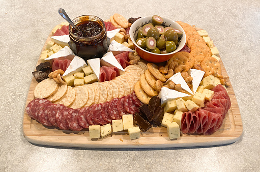 A charcuterie board is an appetizer served on a wooden board. It is eaten straight from the board itself or portioned onto plates. The board features a selection of preserved foods, especially cured meats, as well as cheeses and crackers or bread.
