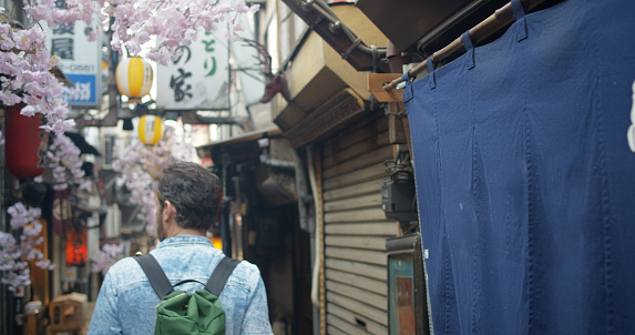 A caucasian male tourist wearing a backpack is walking down an alley in Tokyo