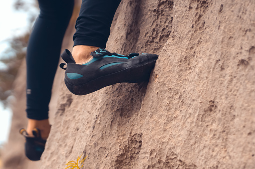 A person climbs the mountain in special climbing shoes, close-up view of the legs with copy space. A woman is engaged in active extreme sports, mountaineering and climbing.