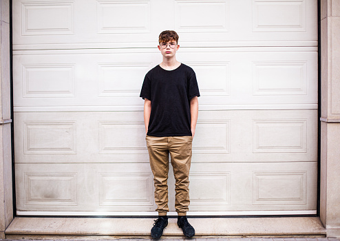 teenage boy standing with hands in pockets in front of garage door