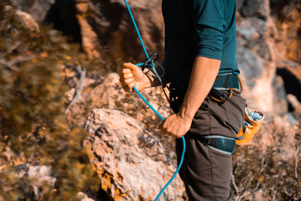 Man is engaged in extreme sports, rock climbing. A young man belays for rock climbing in the mountains outdoors, an athlete controls on a rope during a workout, goes mountain climbing on a sunny day, close-up. jungle gym stock pictures, royalty-free photos & images