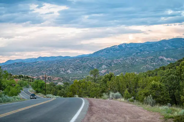 Photo of Sangre De Cristo mountains sunset on Bishops Lodge Road street in Santa Fe New Mexico with car driving, pink sunlight by Tesuque residential community