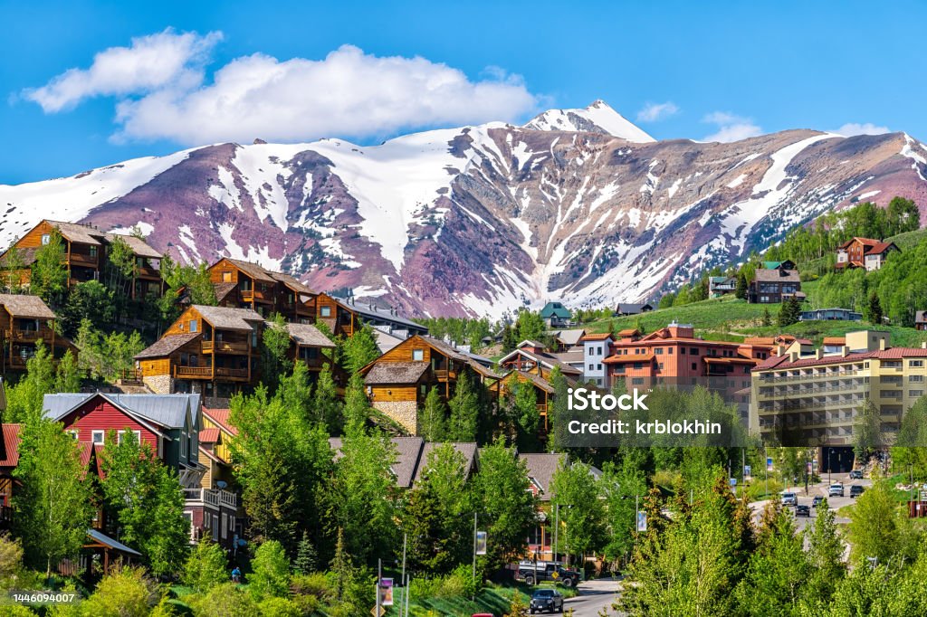 Mount Crested Butte ski resort town, Colorado with houses homes, wooden lodge hotels on hill in summer and green trees by snow-capped mountains in background Colorado Stock Photo