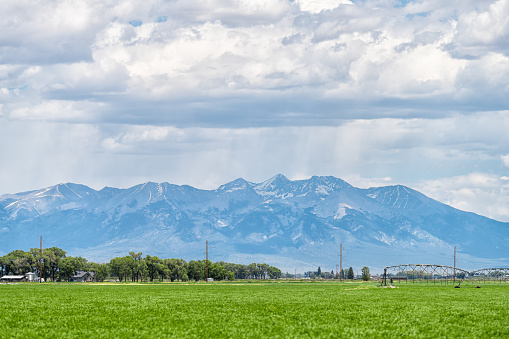 Monte Vista, Colorado countryside in summer on cloudy day with green grass and mountain view by farm equipment irrigation water system for watering crop harvest plants