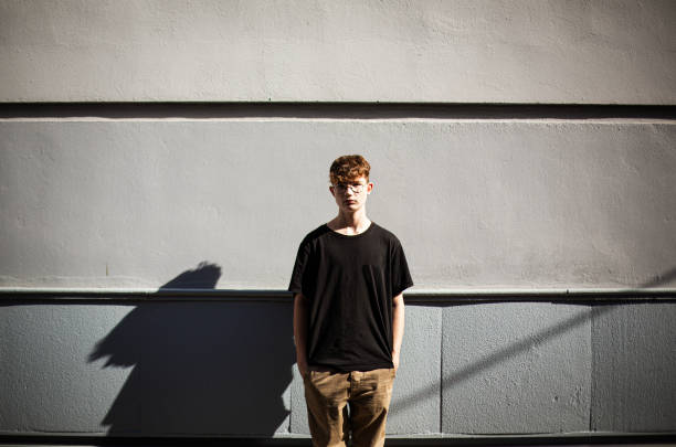 teenage boy standing with hands in pockets in front of a wall