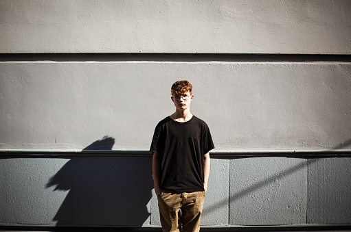 teenage boy standing with hands in pockets in front of a wall