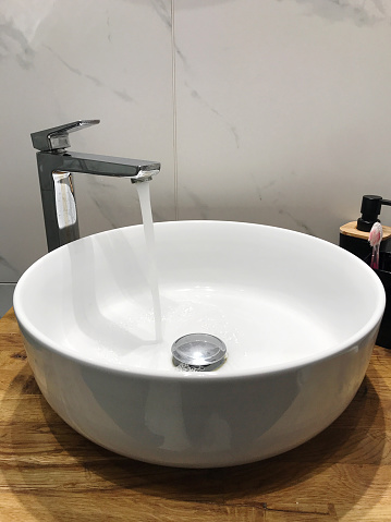 in the bathroom, water runs from the tap into the round wash basin