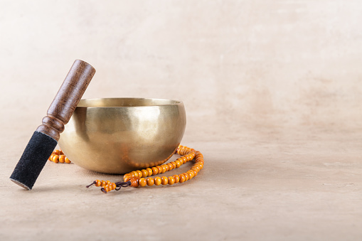 Tibetan singing bowl with stick, mala beads strands used during mantra meditations on beige stone background. Sound healing music instruments for meditation, relaxation, yoga, massage, mental health