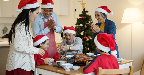 A three generation family, all wearing Santa hats, celebrates Christmas together at home in Taipei.