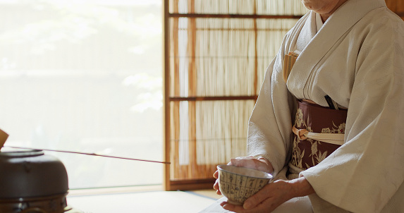 A senior Japanese woman dressed in kimono, acting as the host of a traditional Japanese tea ceremony at a Chashitsu in Tokyo, Japan.