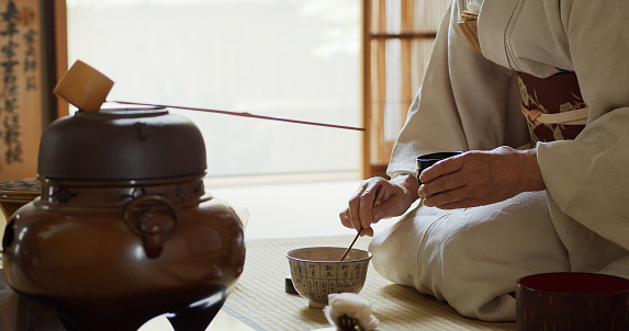 A senior Japanese woman dressed in kimono, acting as the host of a traditional Japanese tea ceremony at a Chashitsu in Tokyo, Japan.