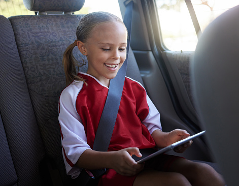 Happy, girl child and with tablet in car smile, browse online and use social media apps while buckled up. Female kid, use digital device or after practice, share winning soccer match or playing game