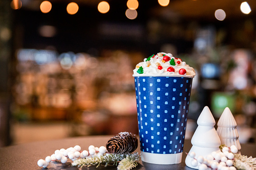A warm hot chocolate drink with whipped cream and sprinkles. Shot inside a coffeeshop with the background blurred. Copy space with room for text included.