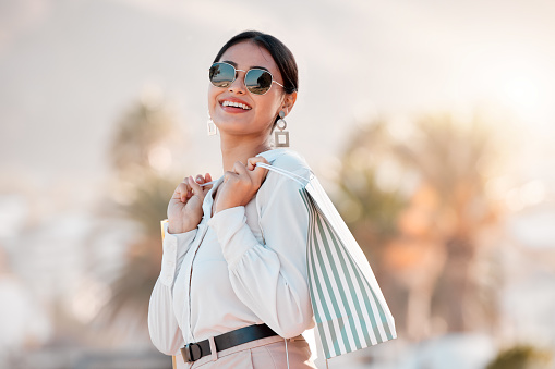 Fashion, style and shopping bags with a woman luxury sunglasses on an urban city street enjoying travel. Stylish, tourism and rich arab female customer or tourist happy about sale discount purchase