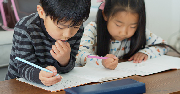 Two young Japanese children completing a kanji worksheet at home.