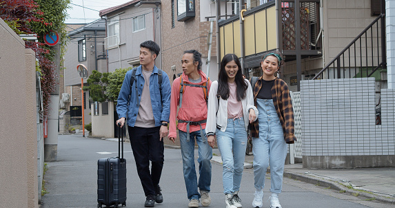 A lively group of young people in their late teens and early twenties who are traveling together are walking down a suburban street in Tokyo, Japan.