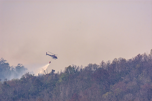 Helicopter dropping water on a forest fire in rugged terrain