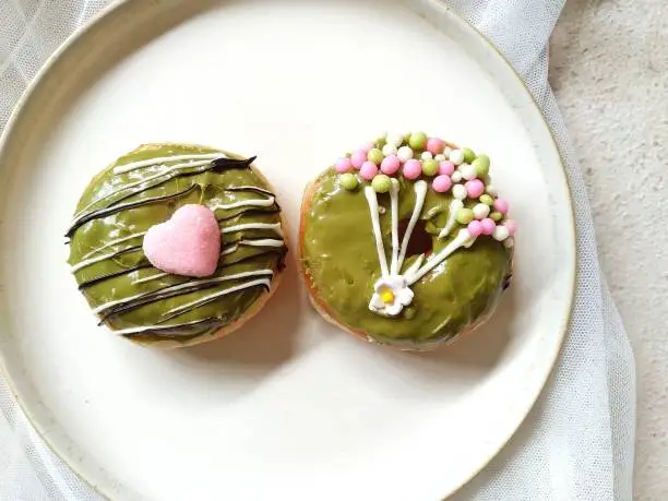 Two donuts with greentea glaze topping on a beige plate