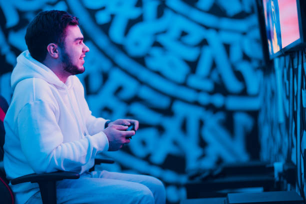 istock Young man plays on game console with gamepad sitting on chair 1446120138