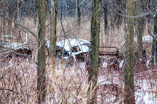 Rusty old junk cars broken in scattered pieces and apparently abandoned - long forgotten in the frozen winter woods.
