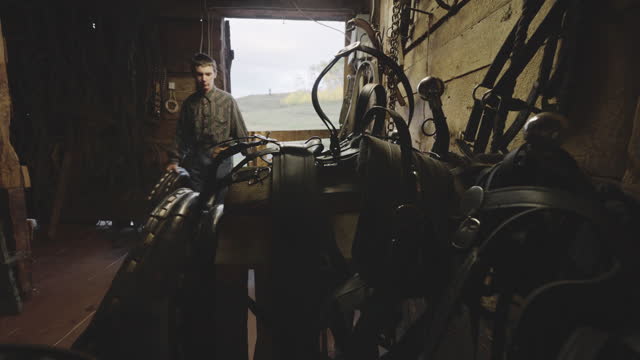 Young White Teenage Farm Boy Replacing Bridle to a Rack in a Tack Room in a Rustic Barn in The Mountains of Southwest Colorado Near Telluride