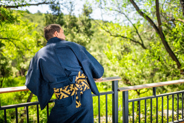 young man in kimono costume traditional clothes standing with back, leaning on railing fence in outdoor garden in japan with nature view - 24241 imagens e fotografias de stock