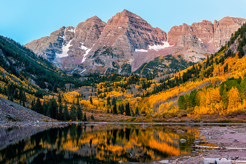 Maroon Bells peak and lake at colorful blue hour sunrise in Aspen, Colorado rocky mountains in October autumn fall season trees reflection on water surface