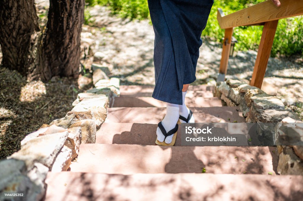 Feet of man in kimono costume, geta tabi shoes socks in outdoor garden with stone steps stairs in Japan by wooden railing Geta Sandal Stock Photo