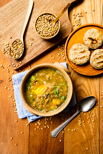 Aerial studio shot of lentil soup with sweet corn on rustic pine wood table. In the photo you can see raw uncooked lentils and ready-to-eat corn bread known in Venezuela as \