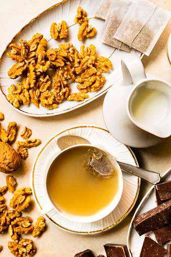 High angle view of prepared chamomile tea with milk and sweet food as chocolate and walnuts \n.Image made in studio using natural soft light from window.\nImage made with a 24 megapixels camera and 35 mm lens f/stop 2.4