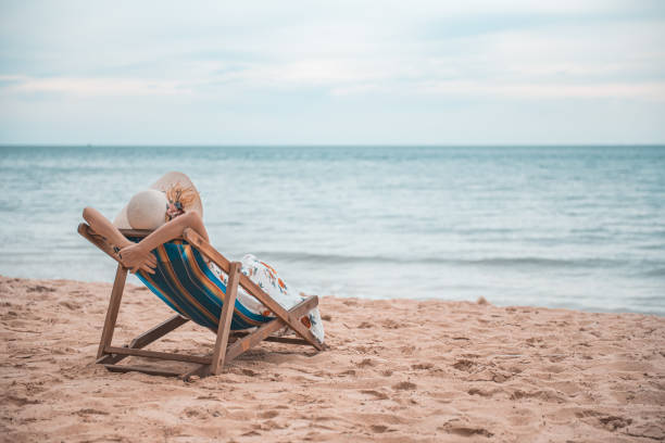 piękna młoda azjatycka kobieta z kapeluszem ramię do góry relaksujące się na krześle plażowym, koncepcja letnich szczęśliwych wakacji. - odprężenie zdjęcia i obrazy z banku zdjęć