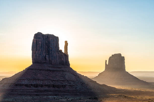 Closeup of east and west mitten buttes and horizon in Monument Valley at sunrise colorful light and sun beam rays behind rock formations in Arizona stock photo