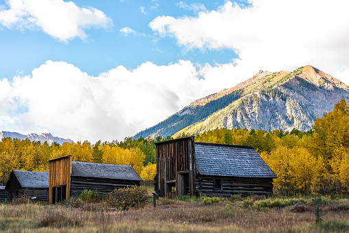 Aspen, Colorado Ashcroft Ghost Town in Castle Creek abandoned wooden house cabins with yellow foliage aspen trees and rocky mountain peak with blue sky