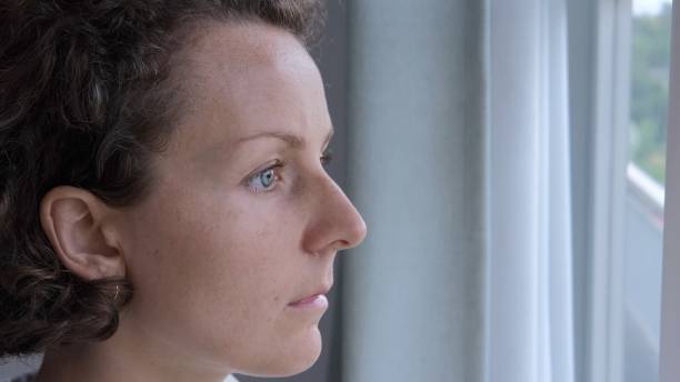 istock A woman standing at the window thoughtfully, attentively with a deep look, never blinking looks out the window. The woman has a beautiful, short haircut. A sad woman is waiting at the window. 1446152205