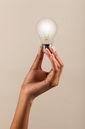 Hand of black woman demonstrating light bulb shining with bright light on beige background