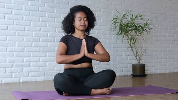 istock Woman practices yoga in a spacious bright room on a mat, develops flexibility, strength, and endurance. Woman in meditation sits on a mat with her hands clasped in front of her in namaste. 1446161581