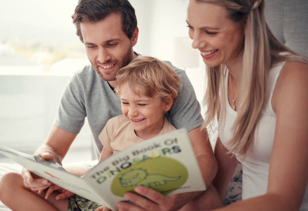 親、子供、家族の家で恐竜の本を読んで、オーストラリアの教育の楽しみ、学習、幸せな発達のために。お母さん、お父さん、子供が遊んだり、学んだり、笑ったりして、面白い動物の話を� - child reading mother book ストックフォトと画像
