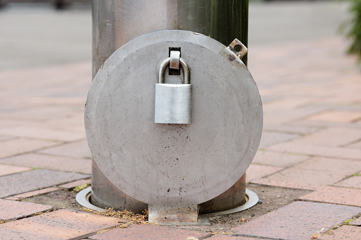 Silver padlock attached to a gray painted metal bollard outdoors.